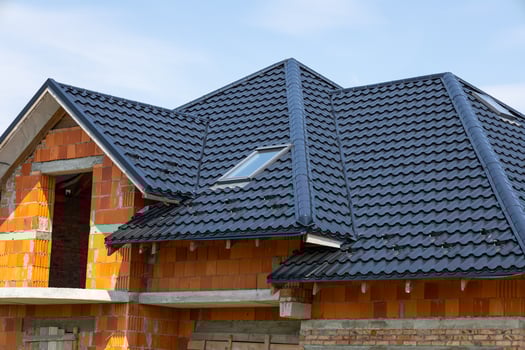 Construction of a house with a black tiled roof and orange brick walls in the framework stage during bright daylight photo