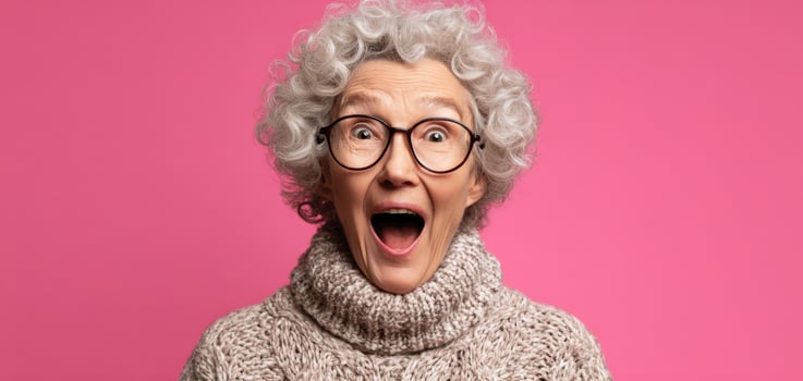 The joyful elderly woman expressing excitement and surprise against a pink background. photo