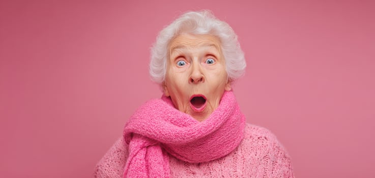 The joyful elderly woman expressing surprise in a vibrant pink setting. photo