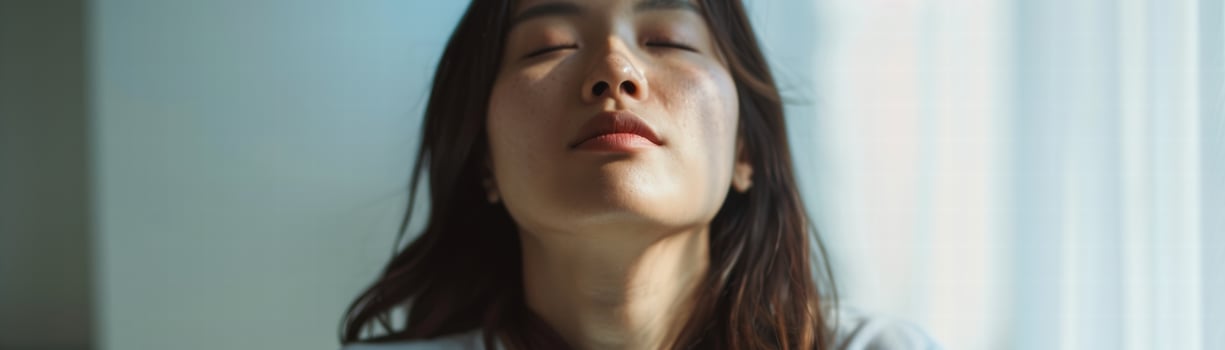 Relaxed young Asian woman with closed eyes enjoying calm moment at home photo