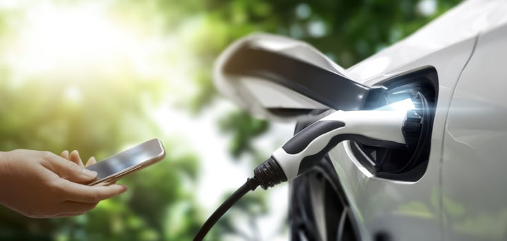 The electric vehicle charging process with smartphone interaction in a green setting. photo