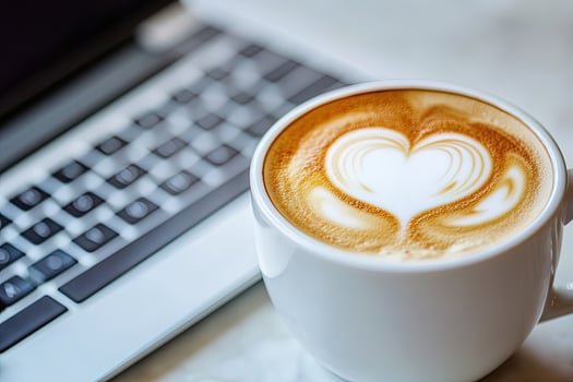 Heart shaped latte art sits warmly next to an open laptop computer photo