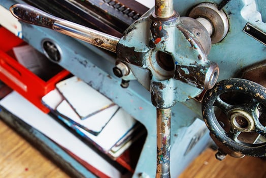 Vintage printmaking press detail with worn crank handle and mechanical components, alongside a stack of inked plates and paper. photo