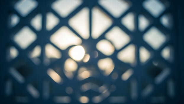A photo of a lattice window with the sun shining through