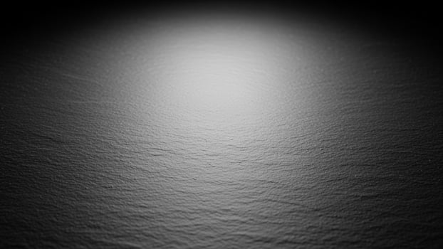 Black and white photo of a dark surface with a light shining through