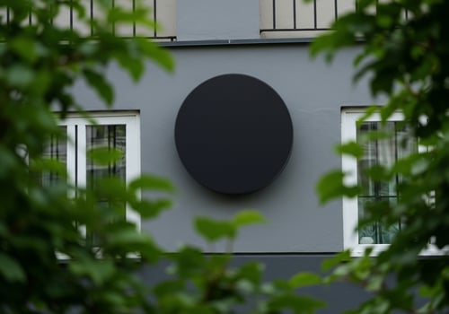 Building facade with dark circle and windows framed by green foliage photo