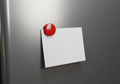 White note card attached to metal surface with red magnet photo
