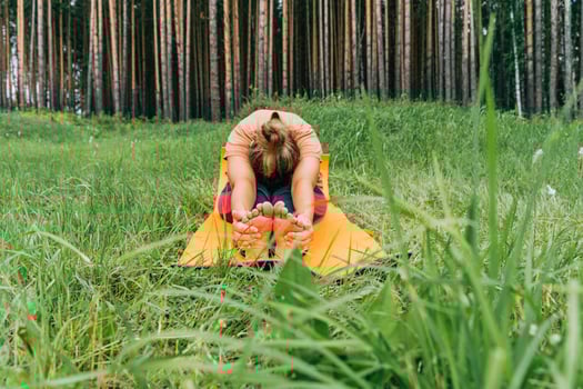 Adult female practicing yoga in forest clearing with green grass photo