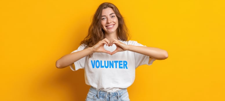 The smiling volunteer making a heart gesture in a bright yellow backdrop. photo