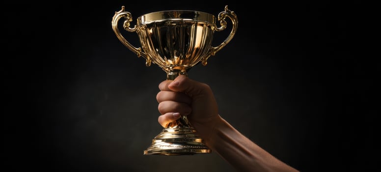 The hand holds a golden trophy symbolizing victory and achievement. photo