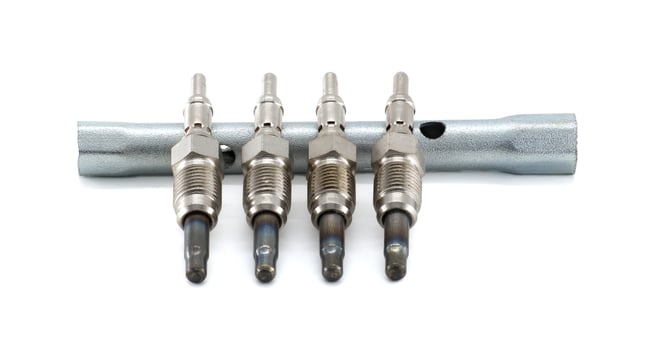 Close-up shot of four glow plugs placed over a wrench on a white backdrop. photo