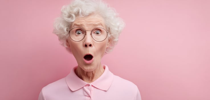 The surprised elderly woman expressing astonishment against a pink background. photo