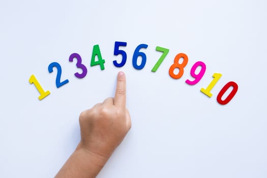 Child pointing at colorful wooden numbers on white background photo