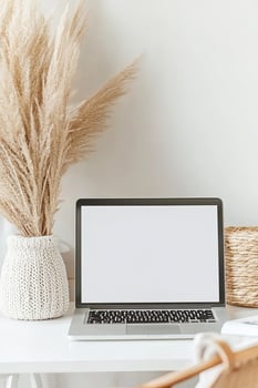 Laptop sits on white desk with pampas grass in neutral interior setting photo