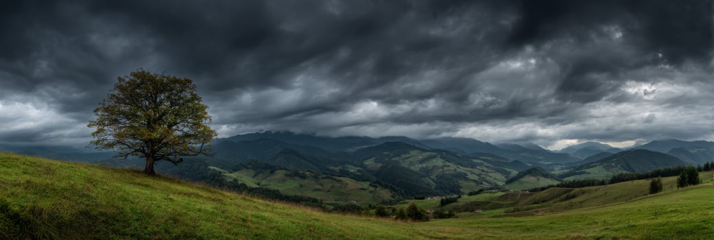 Dramatic Overcast Sky Over Rolling Green Hills with Isolated Tree and Majestic Mountain Range in the Distance photo