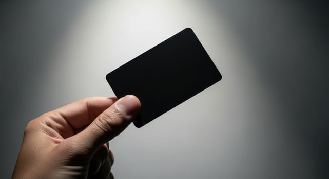 Hand holding a blank black card against a spotlight background photo