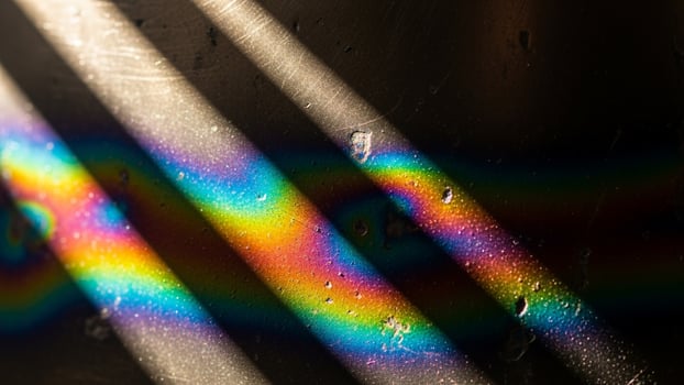 A rainbow colored light shines through the shadows of a wall photo