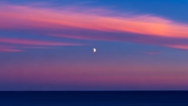 A moon is seen in the sky over the ocean photo