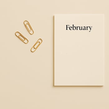 Flat lay of a February calendar page with gold paper clips on a beige surface. Minimalist productivity concept, soft neutral tones, perfect for planning visuals. photo