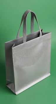 A gray reusable shopping bag with handles stands upright against a solid green background in a studio shot photo