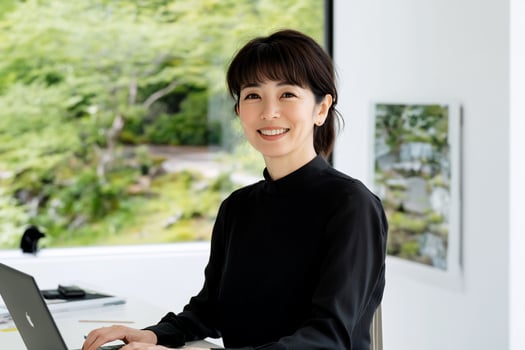 Woman working from home smiling at the camera with natural light and lush greenery outside the window photo