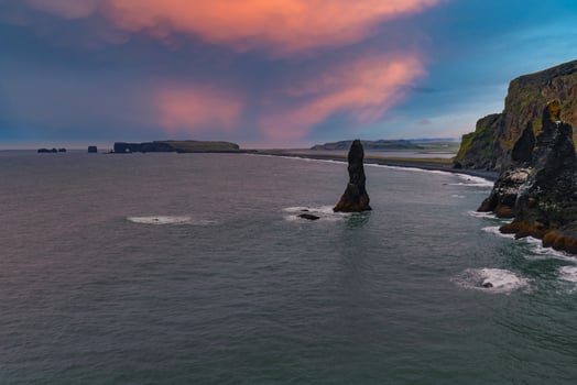 Reynisdrangar sea stacks rise from the ocean near Reynisfjara Black Sand Beach, framed by cliffs and a colorful sunset sky in Iceland. photo