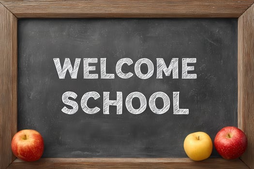 A welcoming chalkboard features the words Welcome School in white chalk. Fresh red and yellow apples are displayed at the bottom, adding a touch of color. photo