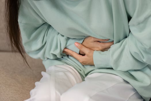 Young woman experiencing abdominal discomfort while sitting on a couch, highlighting health issues and self-awareness. photo