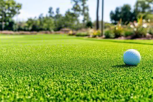 Golf ball on artificial green turf putting field under sunny sky photo