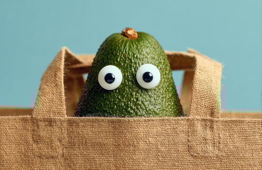 Avocado with googly eyes peeking out of reusable shopping bag photo