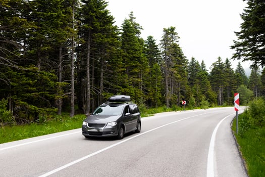 Minivan driving on curved forest road with lush greenery and overcast sky photo