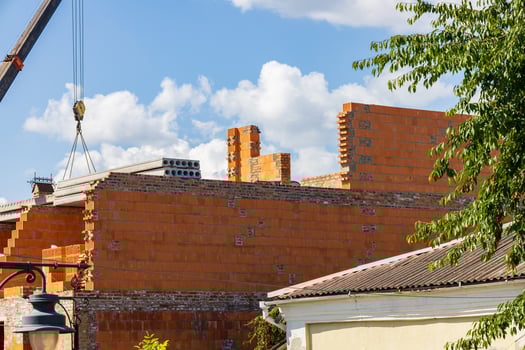 Workers are constructing a new brick building with a crane lifting materials against a backdrop of fluffy clouds and bright sun photo
