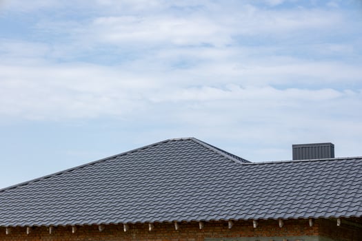 A stylish, sloped roof made of gray tiles stands against a backdrop of a bright blue sky, hinting at a peaceful day photo