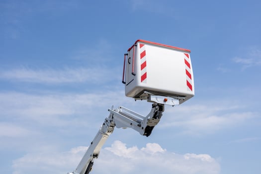 A boom lift is extending toward a high worksite, allowing workers to perform maintenance tasks efficiently against a backdrop of blue skies photo