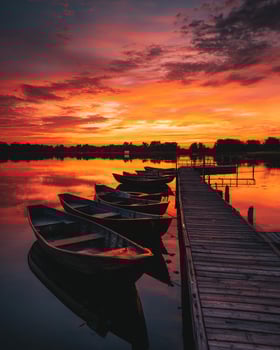 Sunset scene with vivid orange and red sky above peaceful lake where wooden boat dock meets glowing reflective water during golden hour photo