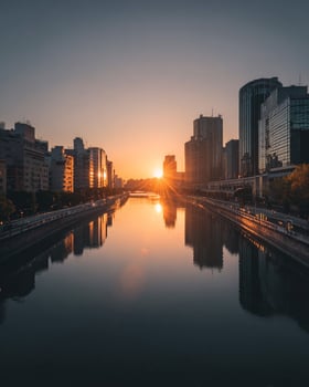 Sunset cityscape showing glowing skyscrapers mirrored on gentle river water with golden hour tones illuminating modern urban environment photo