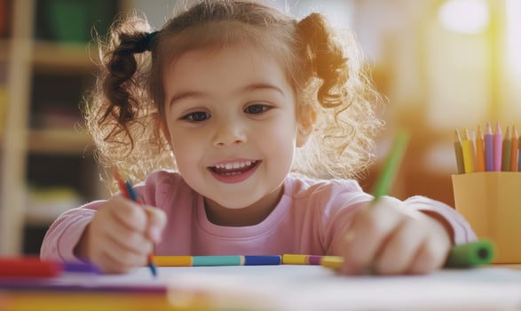 Joyful little girl drawing with colored pencils at a table indoors photo