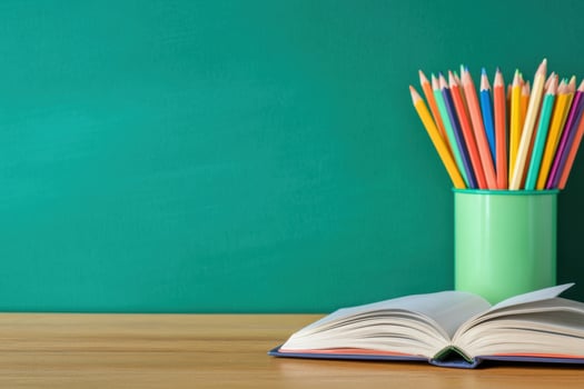 Open book and colored pencils on table top with green background photo
