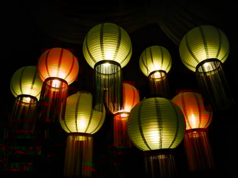 Illuminated paper lanterns with decorative fringe hanging in darkness photo