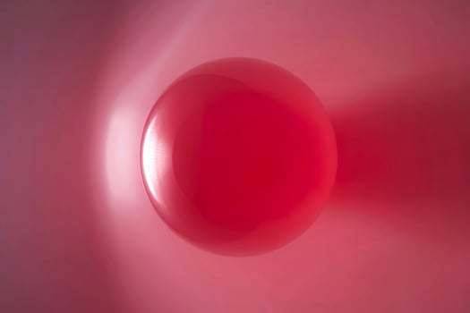 A single glossy red sphere floats against a soft pink and red gradient background photo