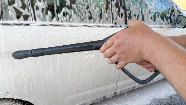 A man with tan skin power washes a car, evoking cleansing rituals, National Clean Up Day, and eco friendly mindfulness photo