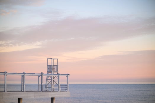 A white wooden pier and a lifeguard stand extend into the calm sea under a beautiful pink and orange sky at sunset. photo