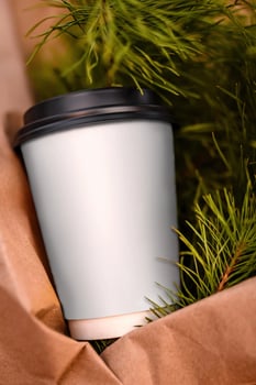 Coffee Cup With Christmas Tree Branches. A blank white takeaway coffee cup is placed inside a brown paper bag with a branch of a green Christmas tree. photo