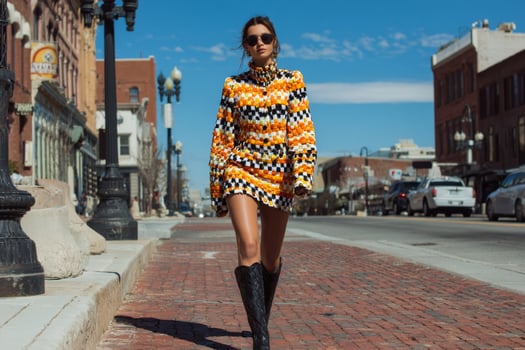 A woman in a colorful dress and boots walking down a street photo