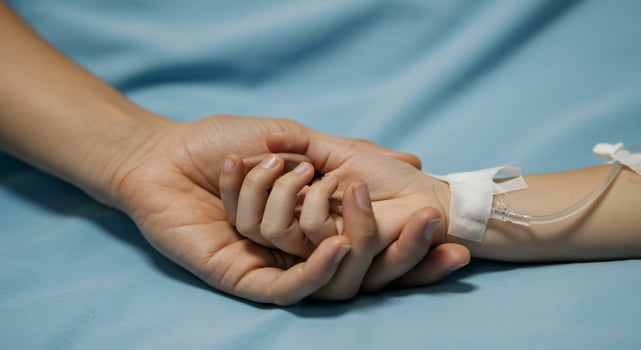 Comforting hand holding child's hand with IV drip on blue hospital bedsheet photo