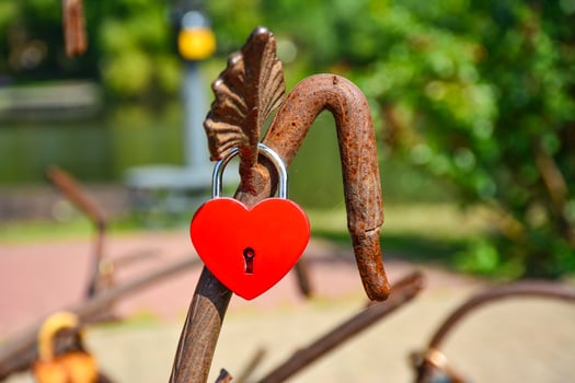 Colorful heart-shaped lock. A bright red heart-shaped lock on an old, rusted metal railing in a city park. Valentines day, love concept. photo