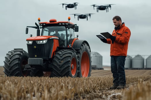 A man in an orange jacket is standing in front of a tractor with a drone flying over it photo