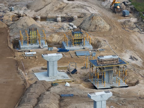 Active construction site on Riga to Jelgava road with concrete pillars, scaffolding, heavy machinery, and organized areas for materials and equipment. photo