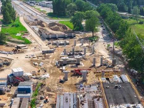 Large scale construction site on Riga to Jelgava road with concrete pillars, heavy machinery, and materials. Surrounded by greenery, with a partially built road visible. photo
