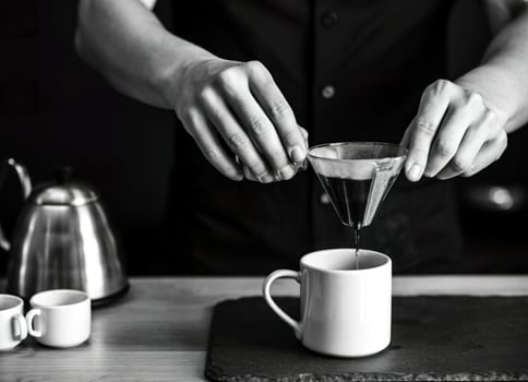 Barista carefully pours coffee through a filter into a white mug photo